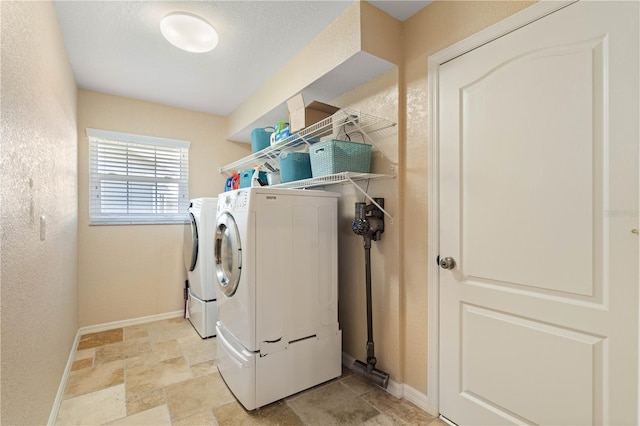 clothes washing area featuring independent washer and dryer, laundry area, stone finish flooring, a textured wall, and baseboards