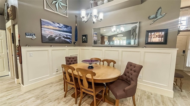 dining area with a chandelier, light wood-style flooring, a decorative wall, and wainscoting