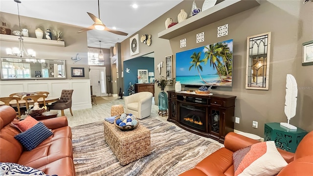 living room with a glass covered fireplace, wood finished floors, and ceiling fan with notable chandelier