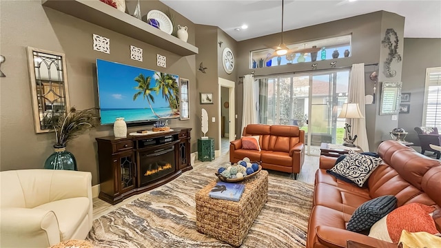 living room with recessed lighting, a towering ceiling, wood finished floors, baseboards, and a glass covered fireplace
