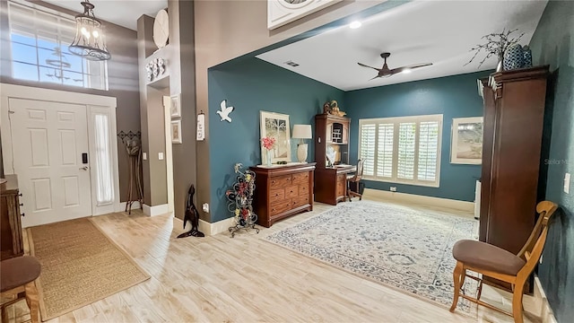 entryway with baseboards, visible vents, ceiling fan with notable chandelier, wood finished floors, and a high ceiling