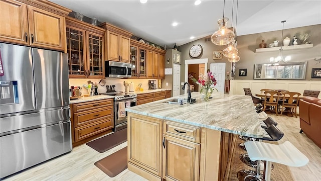 kitchen featuring light wood-style flooring, a sink, light stone countertops, a breakfast bar, and appliances with stainless steel finishes