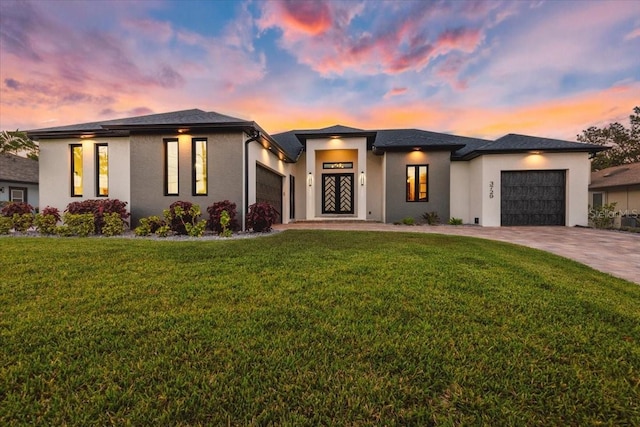 prairie-style home with a yard, decorative driveway, stucco siding, and a garage