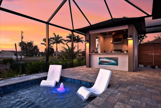 pool at dusk with an outdoor kitchen, a lanai, and a patio area
