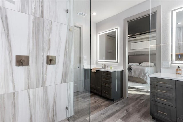 ensuite bathroom featuring connected bathroom, a walk in shower, vanity, wood finished floors, and visible vents