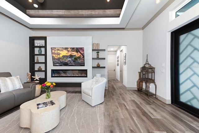 living room with baseboards, a raised ceiling, wood finished floors, and built in shelves