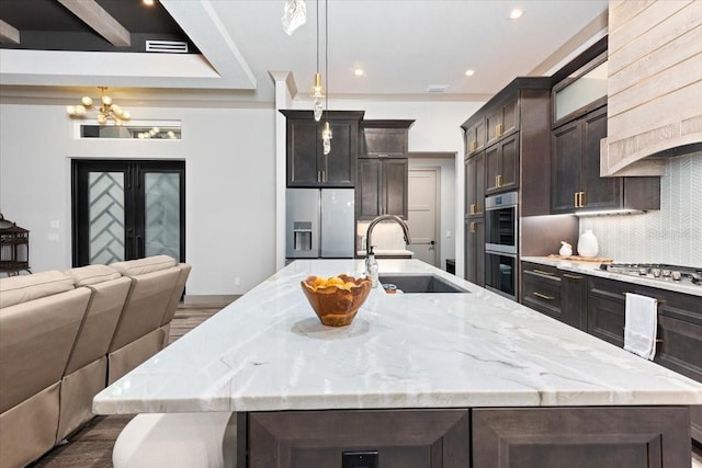 kitchen featuring a large island with sink, a sink, a notable chandelier, stainless steel appliances, and open floor plan