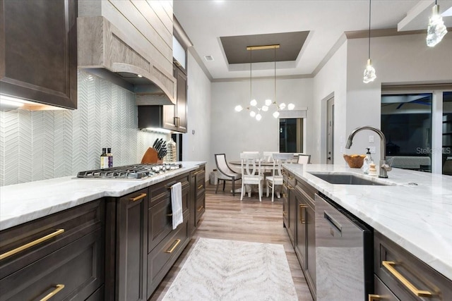 kitchen with decorative backsplash, appliances with stainless steel finishes, a sink, premium range hood, and light stone counters