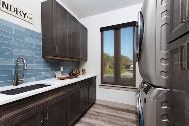 laundry room with cabinet space, stacked washer and dryer, a sink, light wood-style floors, and baseboards