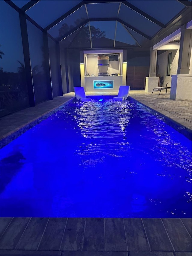 pool at twilight featuring a patio, glass enclosure, and an outdoor pool