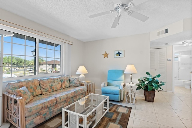living area featuring ceiling fan, a textured ceiling, visible vents, and light tile patterned floors