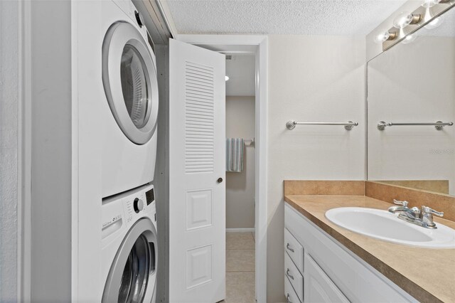 bathroom with stacked washer and dryer, a textured ceiling, vanity, tile patterned floors, and baseboards