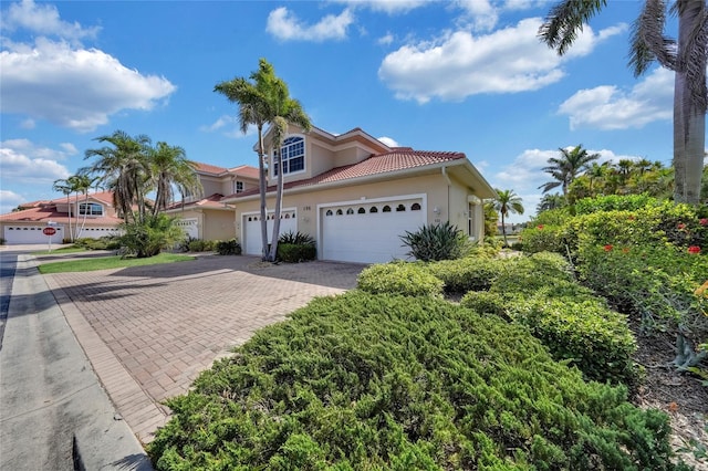 mediterranean / spanish-style house with stucco siding, a tile roof, a garage, and decorative driveway