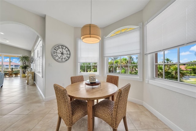 dining area featuring lofted ceiling, baseboards, arched walkways, and light tile patterned floors