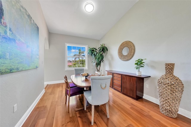 dining room featuring baseboards, light wood finished floors, and vaulted ceiling