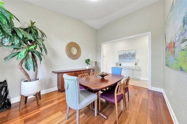 dining space featuring lofted ceiling, baseboards, and light wood-style floors