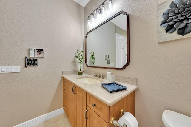 half bathroom featuring vanity, toilet, a textured wall, and tile patterned floors