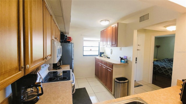 kitchen with light tile patterned flooring, visible vents, white appliances, brown cabinetry, and light countertops
