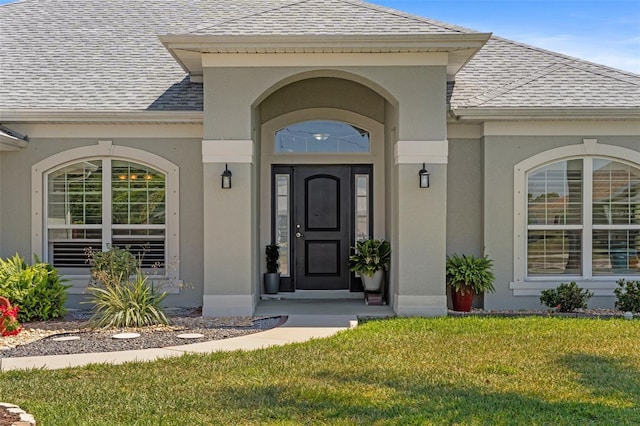 27147 Guapore Dr, Punta Gorda, FL 33983 - view of exterior entry featuring a lawn, roof with shingles, and stucco siding