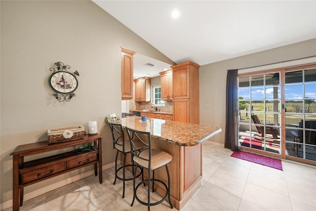 kitchen featuring vaulted ceiling, a sink, light stone countertops, a peninsula, and a kitchen bar