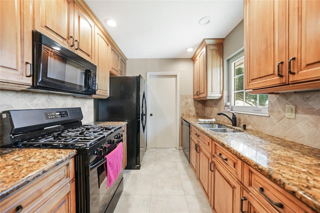 kitchen with a sink, light tile patterned flooring, decorative backsplash, light stone countertops, and black appliances