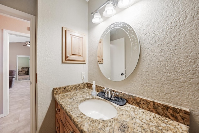 bathroom with a textured wall, vanity, and ceiling fan