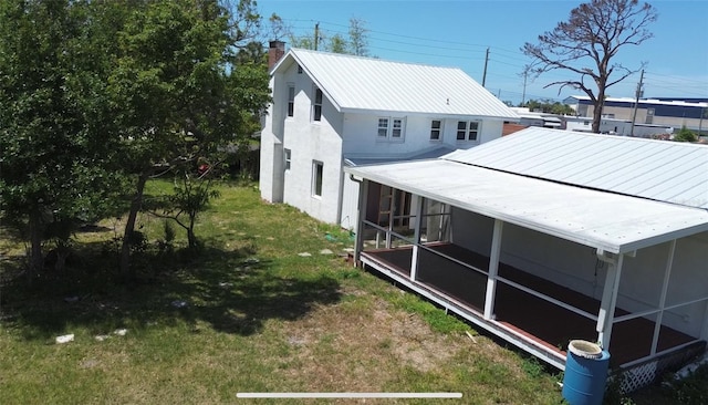rear view of house featuring a chimney, a lawn, metal roof, stucco siding, and a sunroom