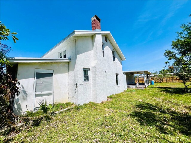 view of side of home with fence, a lawn, a chimney, and stucco siding