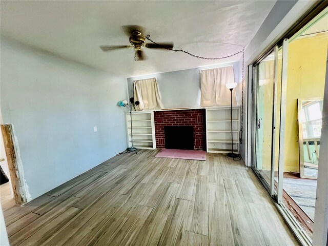 unfurnished living room with wood finished floors, a brick fireplace, and a ceiling fan