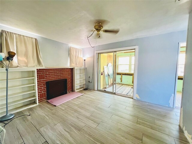 unfurnished living room with a brick fireplace, wood finished floors, and a ceiling fan