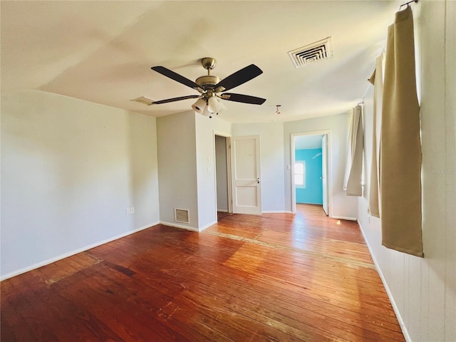 spare room featuring wood-type flooring, visible vents, a ceiling fan, and baseboards