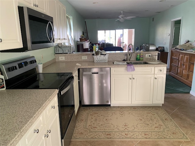 kitchen featuring a peninsula, a sink, open floor plan, a ceiling fan, and appliances with stainless steel finishes