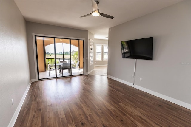 unfurnished living room featuring a ceiling fan, baseboards, and dark wood-type flooring