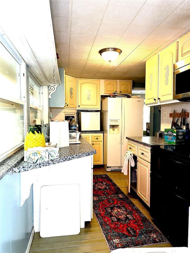 kitchen featuring stainless steel microwave, dark countertops, white fridge with ice dispenser, and wood finished floors