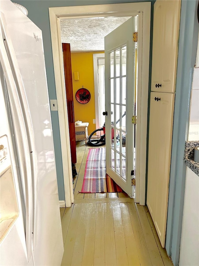 doorway to outside with a textured ceiling, light wood-style flooring, and french doors