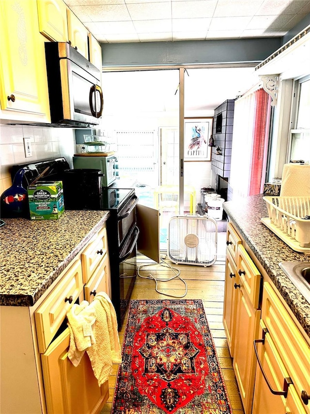kitchen featuring stainless steel microwave, backsplash, a wealth of natural light, and black range with electric stovetop