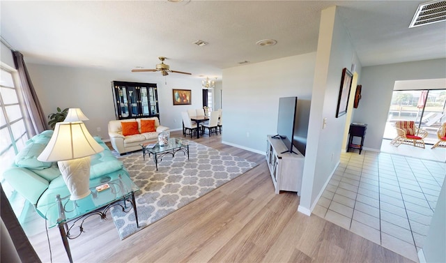 living room featuring light wood-style flooring, visible vents, baseboards, and ceiling fan with notable chandelier