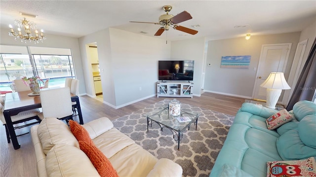 living room featuring baseboards, wood finished floors, visible vents, and ceiling fan with notable chandelier