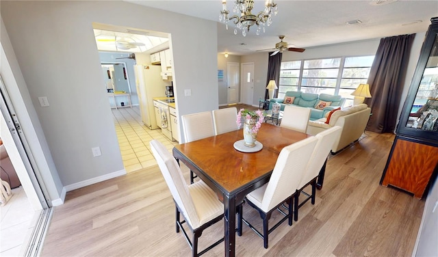 dining space featuring ceiling fan with notable chandelier, baseboards, and light wood-type flooring