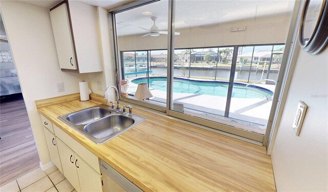 kitchen featuring a sink, a water view, white cabinetry, a ceiling fan, and butcher block counters