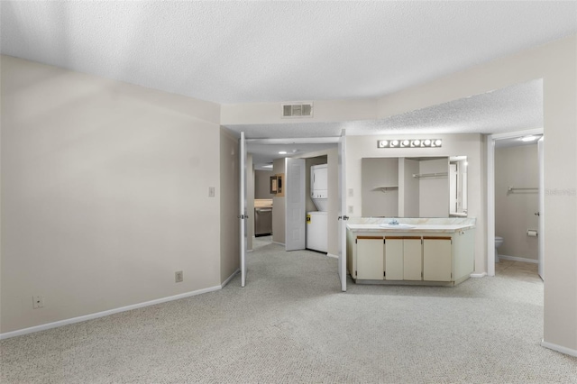 19505 Quesada Ave Unit A204, Port Charlotte, FL 33948 - unfurnished living room featuring a textured ceiling, stacked washer / drying machine, visible vents, baseboards, and light carpet