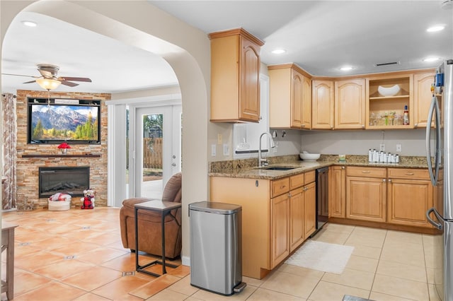 kitchen featuring freestanding refrigerator, arched walkways, light stone counters, a sink, and light tile patterned floors