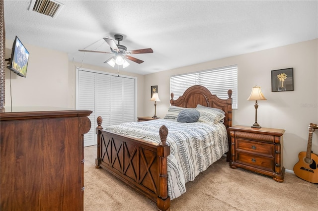 bedroom featuring visible vents, a closet, light carpet, ceiling fan, and a textured ceiling