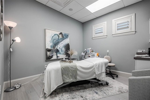 bedroom with wood finished floors, a drop ceiling, and baseboards
