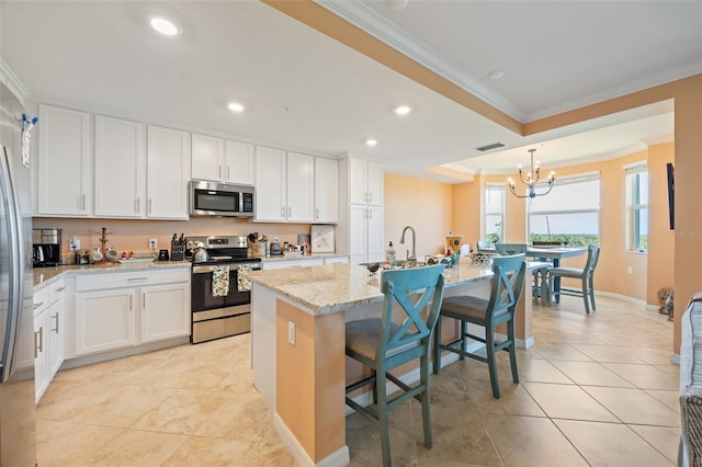 kitchen with stainless steel appliances, a notable chandelier, a center island with sink, crown molding, and white cabinetry