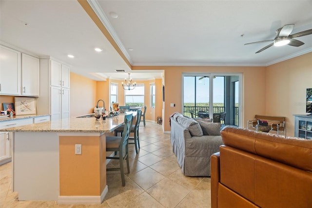 kitchen featuring crown molding, white cabinets, a sink, open floor plan, and a kitchen bar