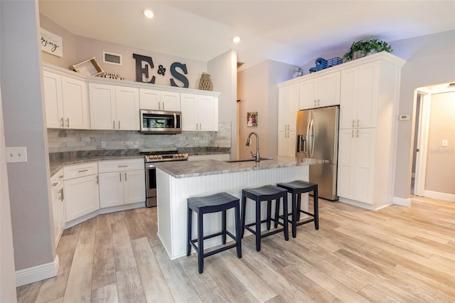 kitchen featuring a kitchen island with sink, a sink, tasteful backsplash, visible vents, and appliances with stainless steel finishes