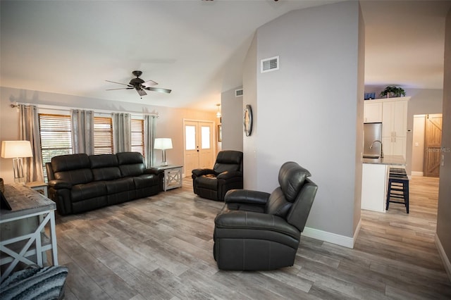 living area featuring visible vents, baseboards, light wood-type flooring, vaulted ceiling, and a ceiling fan