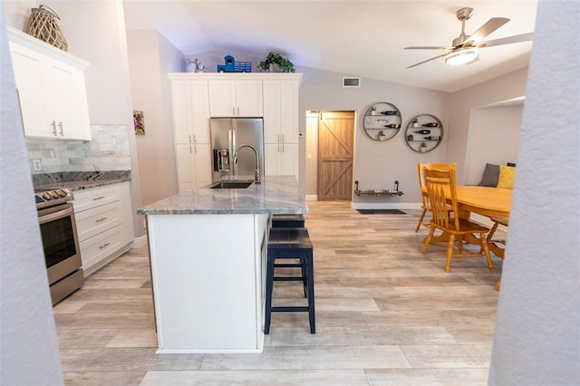 kitchen featuring a breakfast bar area, appliances with stainless steel finishes, white cabinets, a sink, and lofted ceiling