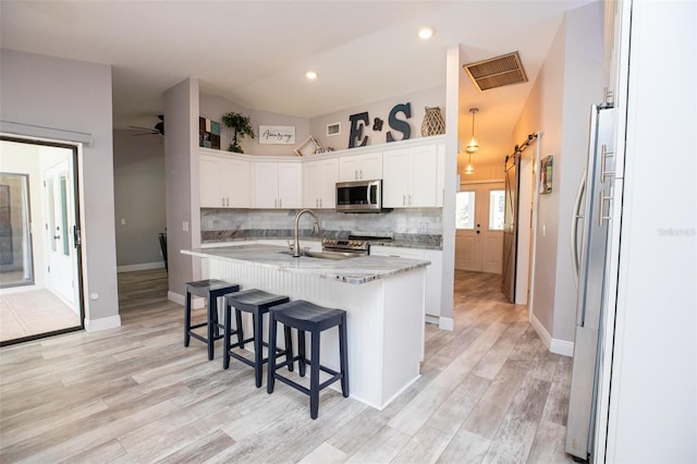 kitchen featuring a sink, stainless steel appliances, a kitchen breakfast bar, white cabinetry, and an island with sink